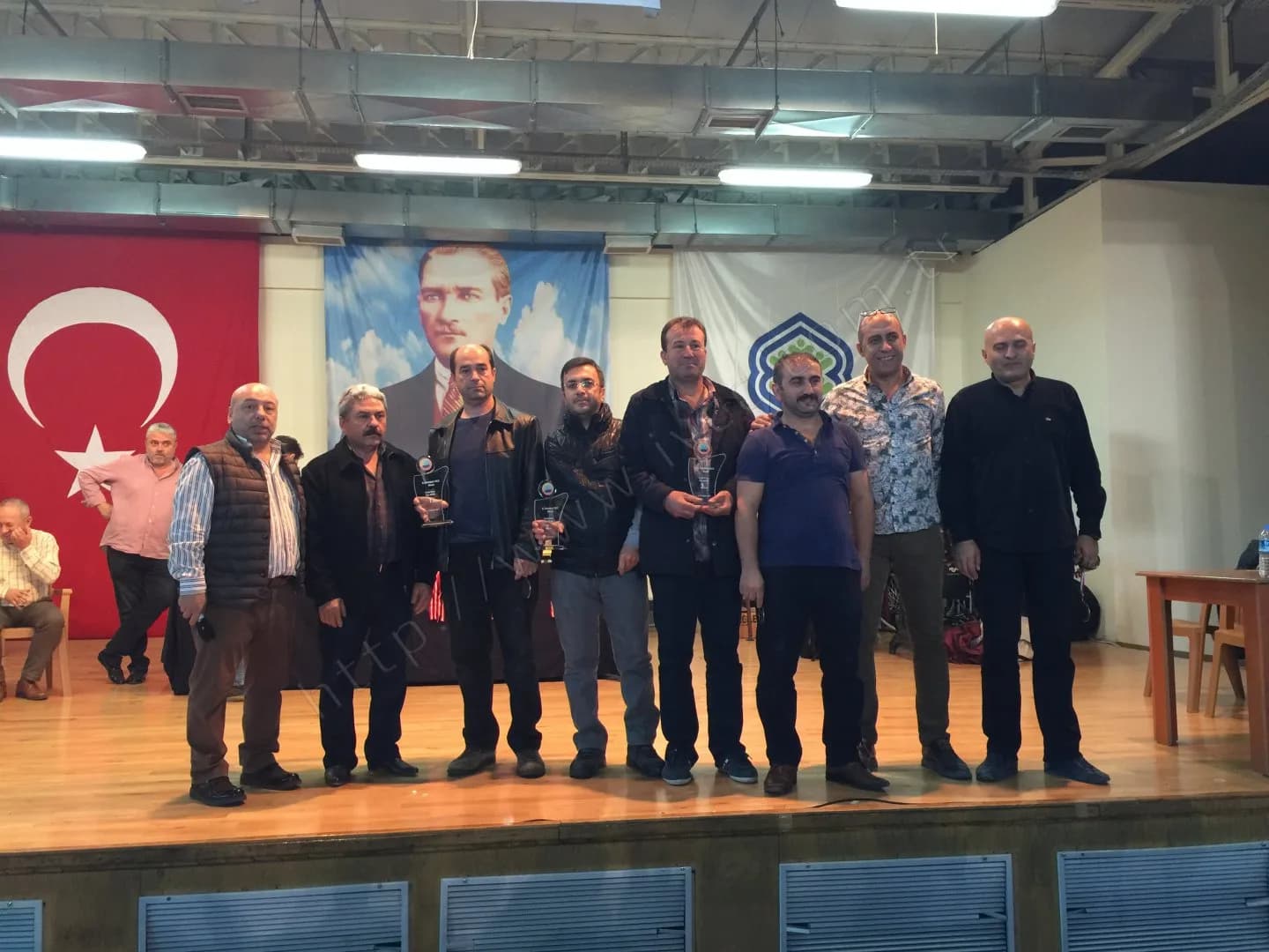IYCC 2017 ödül töreninde dokuz kişi sahnede sıralanmış, üç kişi cam plaket tutuyor, sağda boş bir masa