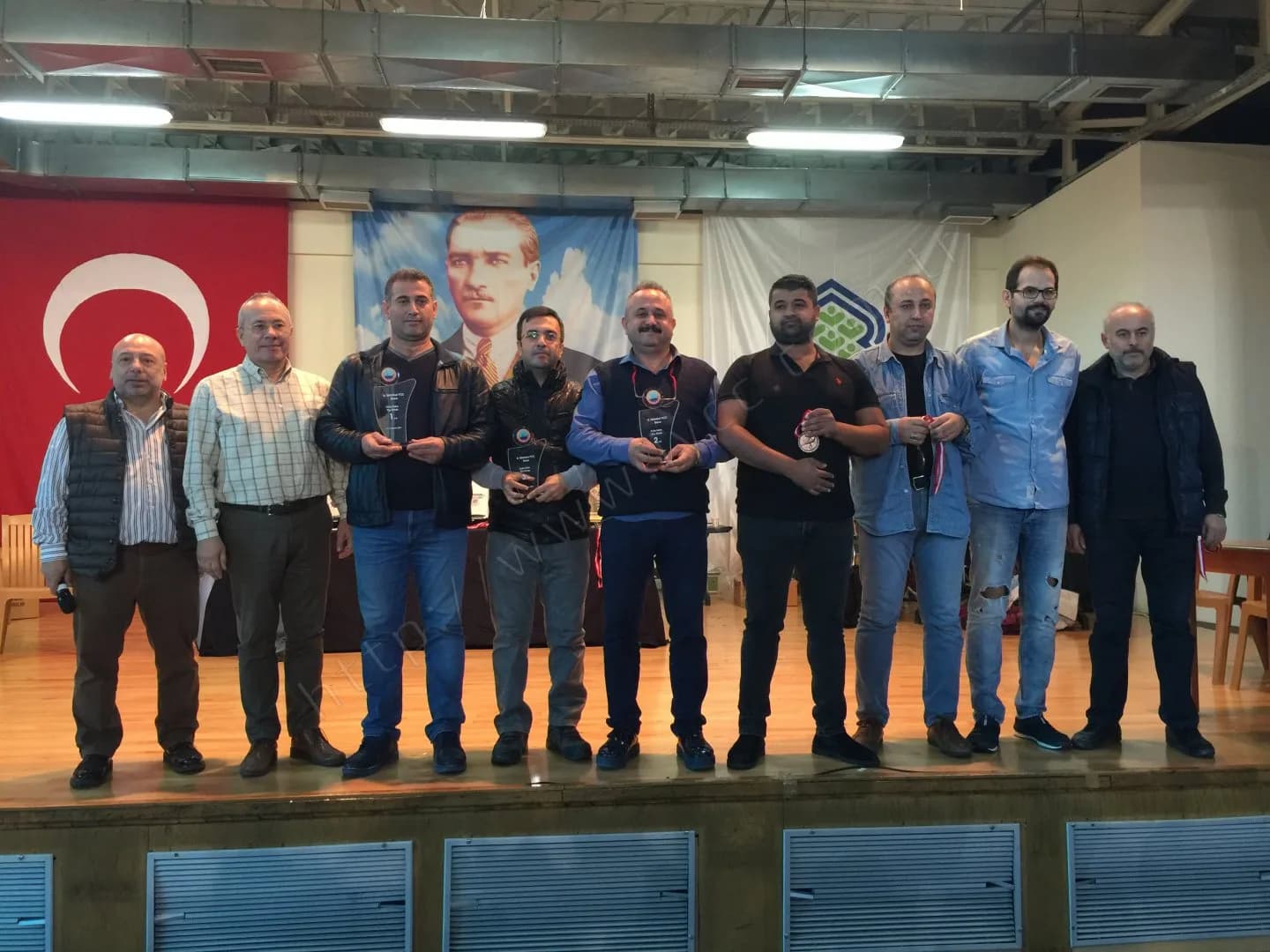 IYCC 2017 ödül töreninde sahnede on kişi; üçü 1, 2 ve 3 numaralı cam plaket, biri madalya tutuyor