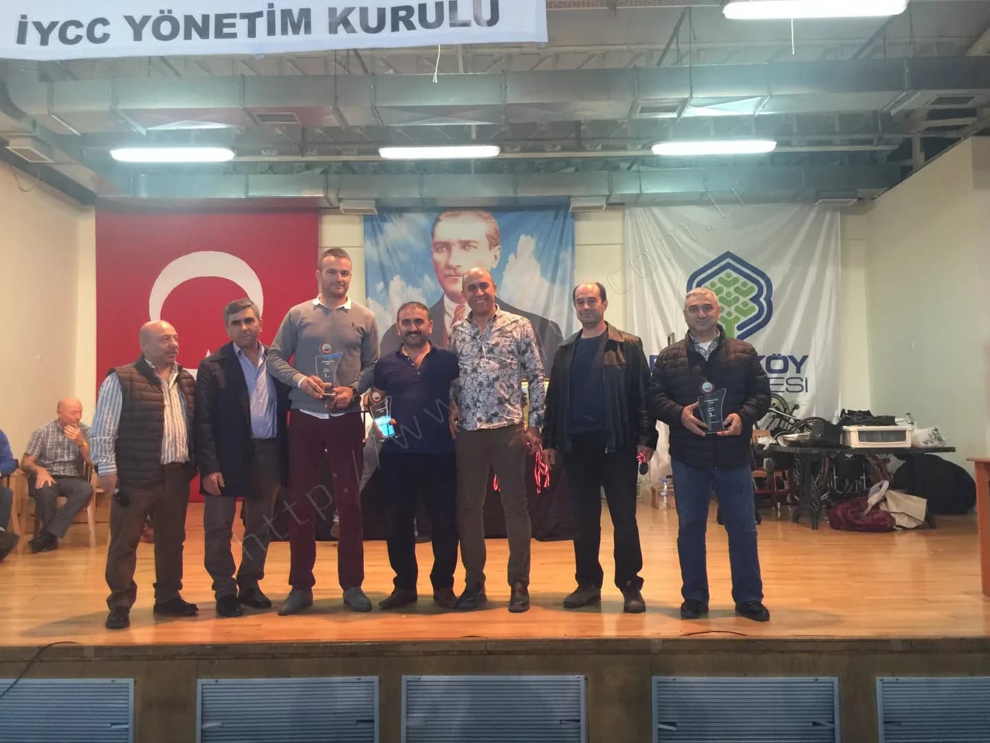 IYCC 2017 ödül töreninde Yönetim Kurulu pankartı altında sekiz kişi, üç kişinin elinde cam plaket