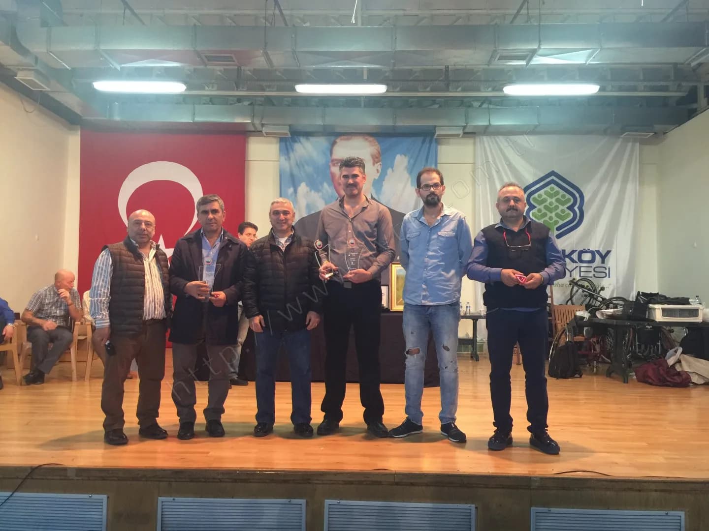 IYCC 2017 ödül töreninde sahnede altı kişi, ikisi cam plaket tutuyor, arkada çerçeveli tablo görülüyor