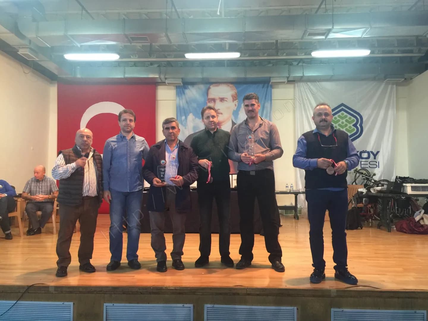 IYCC 2017 ödül töreninde sahnede altı kişi; biri 2 yazılı cam plaket, ikisi madalya tutuyor
