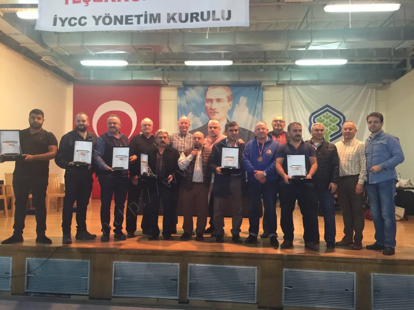 IYCC 2017 ödül töreninin toplu fotoğrafında ortadaki kişi mikrofonla konuşuyor, çevresinde plaketli katılımcılar