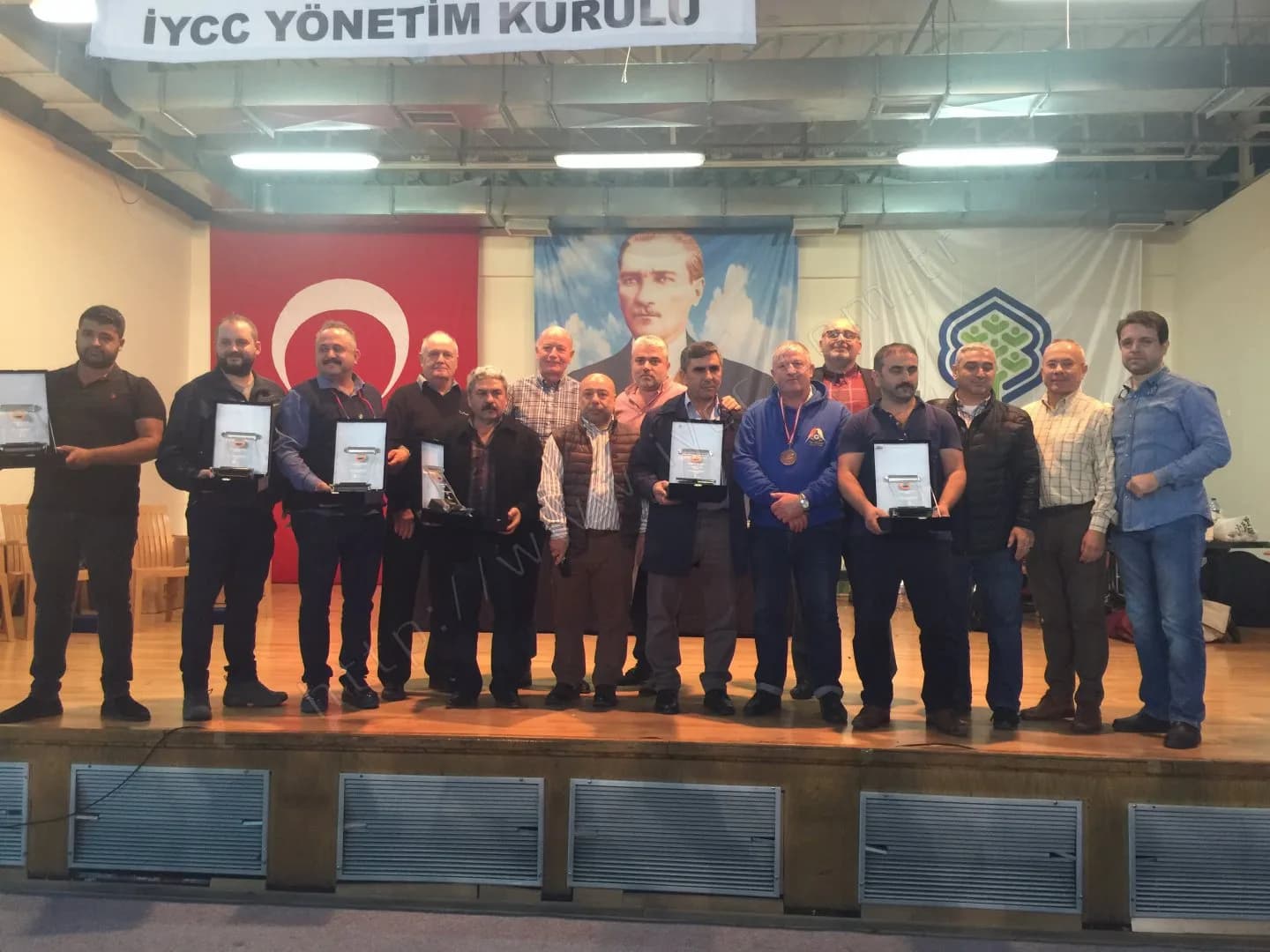 IYCC 2017 ödül töreninde plaket ve madalyalarıyla sahnede objektife bakan on yedi kişilik toplu fotoğraf