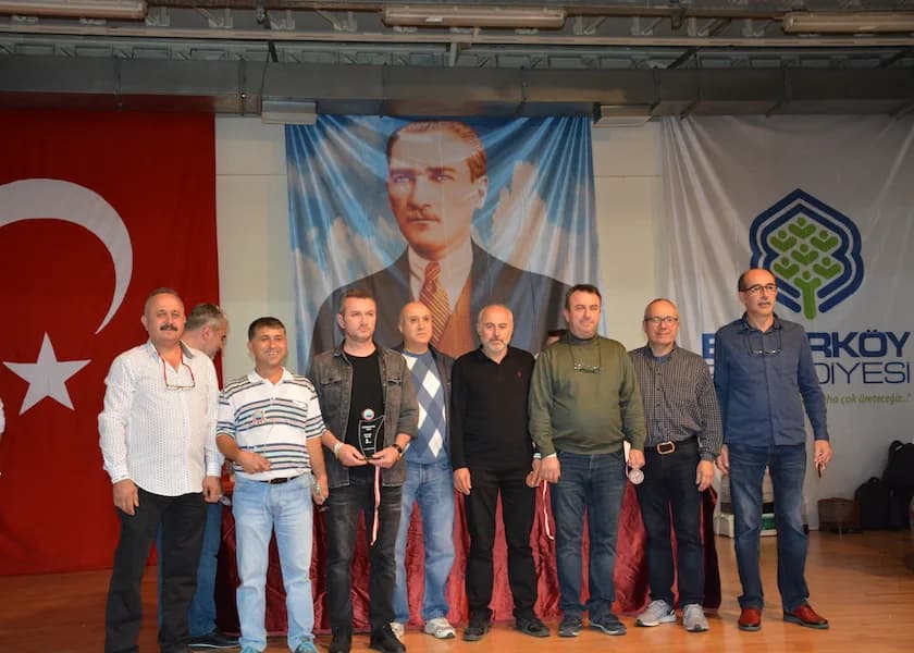 Nine men stand before a municipality banner and an Atatürk portrait at the IYCC 2018 awards, one holding a trophy