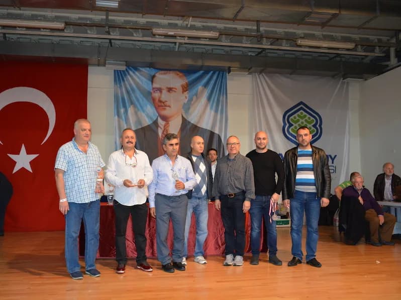 Eight men pose on stage at the IYCC 2018 final, two holding small crystal trophies, with seated spectators on the right