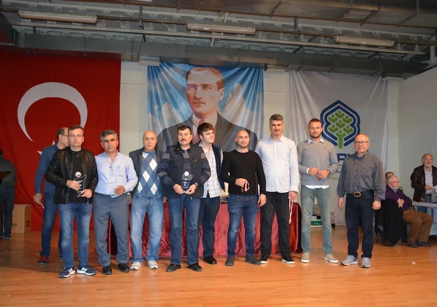 An eleven-person group lines the stage at the IYCC 2018 awards, two holding trophies, with spectators seated on the right