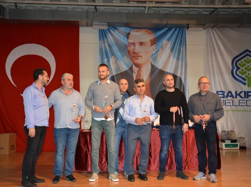 Seven men pose with ribboned medals and trophies at the IYCC 2018 awards; the man in the centre holds two trophies
