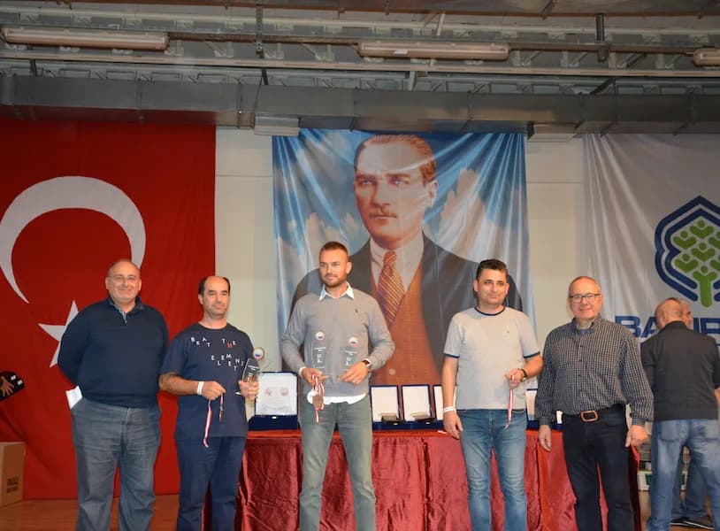 Five men stand before a table of boxed plaques at the IYCC 2018 awards, the one in the middle holding two trophies