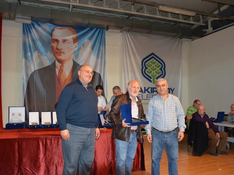 A man in a leather jacket receives a boxed plaque at the IYCC 2018 awards, flanked by two men, award table on the left