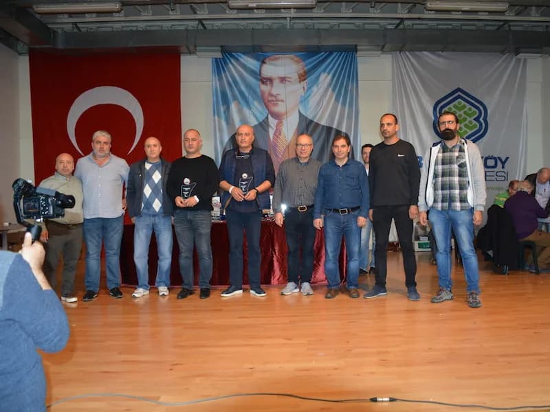 A group of ten, two holding trophies, poses on stage at the IYCC 2018 awards while a camera operator films in front