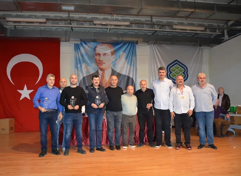 A large group on stage at the IYCC 2018 awards; three men on the left hold trophies and another wears a medal