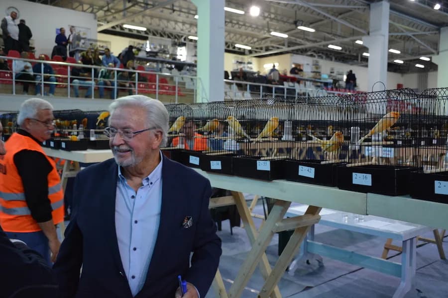 IYCC 2018 yarışmasında lacivert ceketli, elinde kalem olan bir kişi 2-42 ve 2-16 numaralı kafes sırasının önünde gülümsüyor