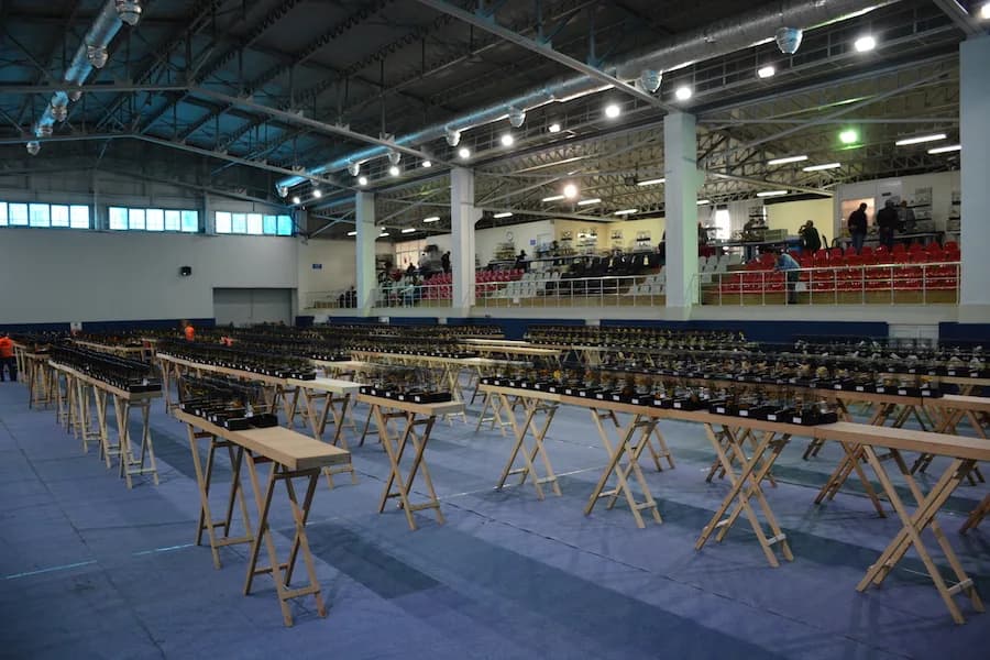 IYCC 2018 yarışması öncesi spor salonunda tahta sehpalar üzerinde uzanan kafes sıraları ve kırmızı-beyaz tribün koltukları